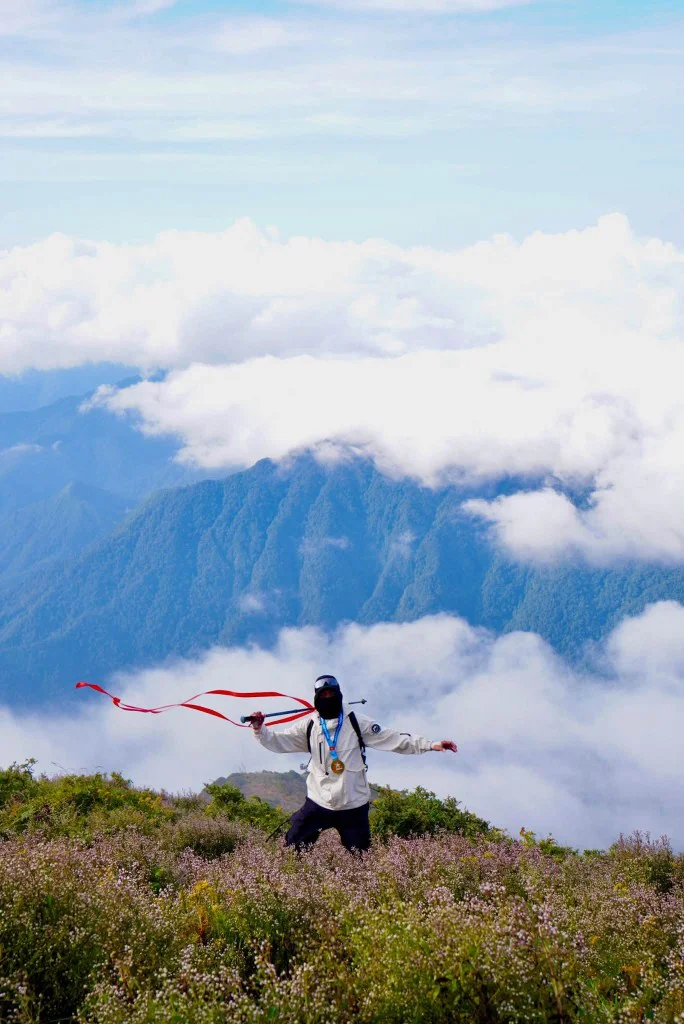 Trekker áo khoác trắng giơ dải ruy băng đỏ trên đỉnh Tà Chì Nhù, phía dưới là biển mây