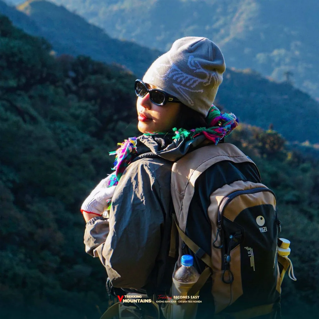 Nữ trekker đội mũ len, đeo balo nhìn về dãy núi rừng Tà Xùa trên hành trình trekking Sa Mu