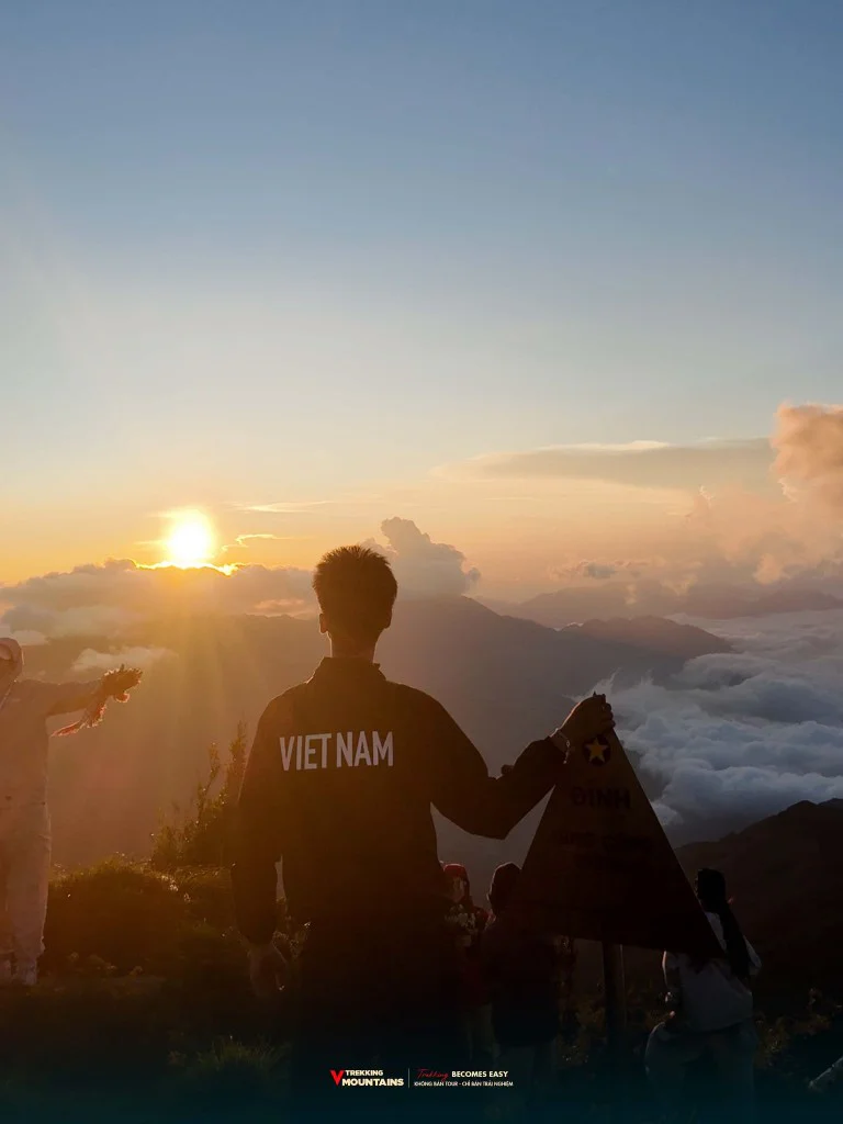 Trekker đứng cạnh cột mốc đỉnh Lùng Cúng 2913m ngắm mặt trời trên biển mây