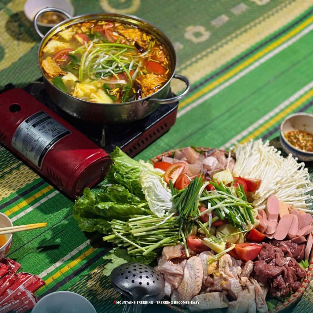 Nồi lẩu trên bếp ga cạnh mẹt rau, nấm, cà chua và thịt sống
