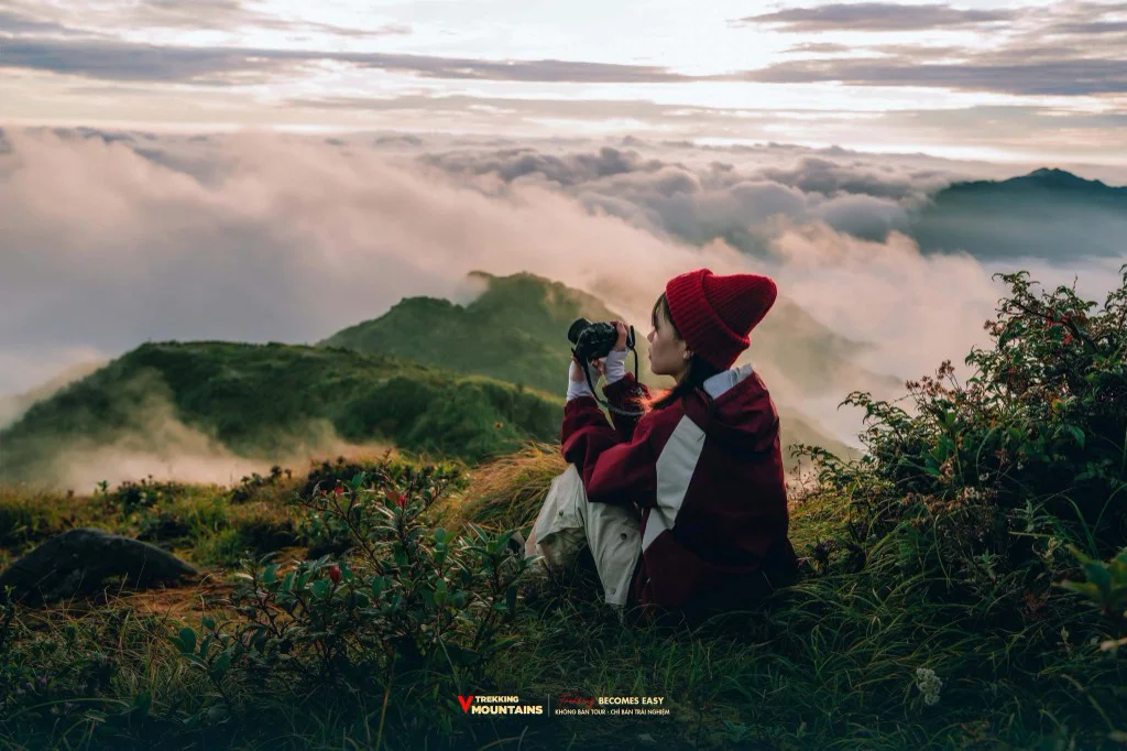 Cô gái đội mũ len đỏ cầm máy ảnh chụp biển mây trên sườn núi Lùng Cúng