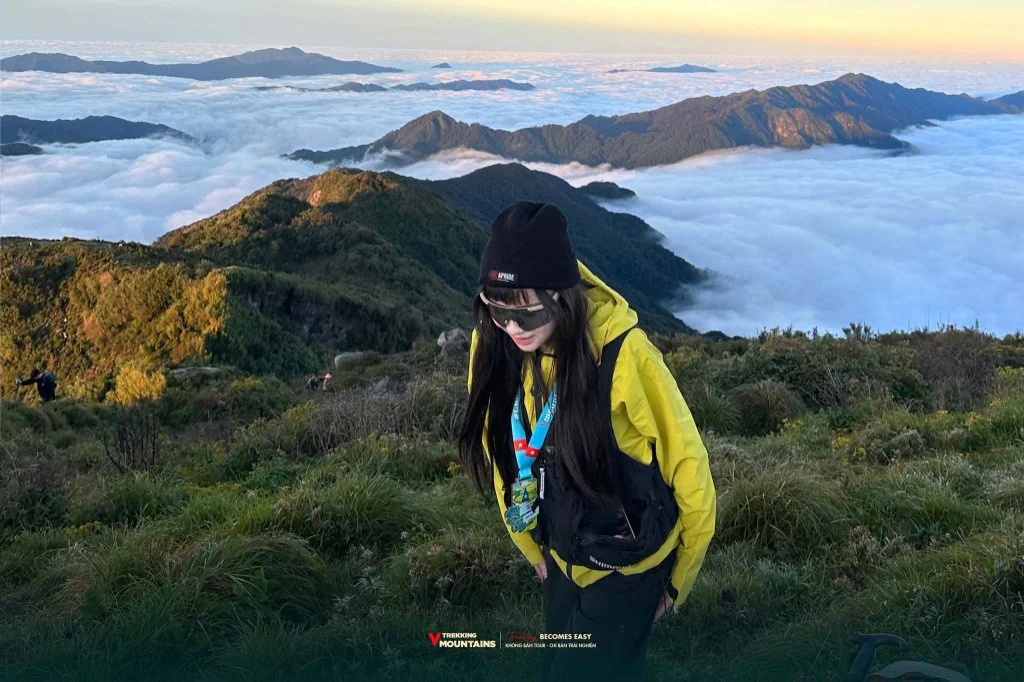 Nữ trekker áo vàng đeo huy chương trên sườn núi Lùng Cúng phía trên biển mây